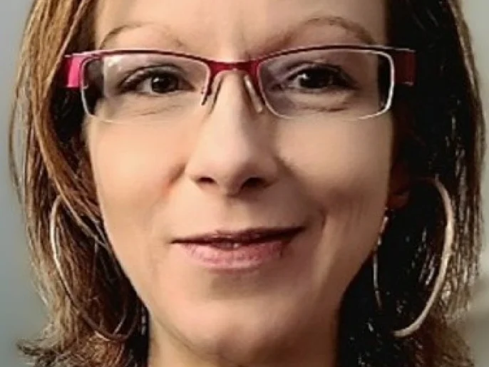 Lächelnde Frau mit schulterlangem Haar und roter Brille.