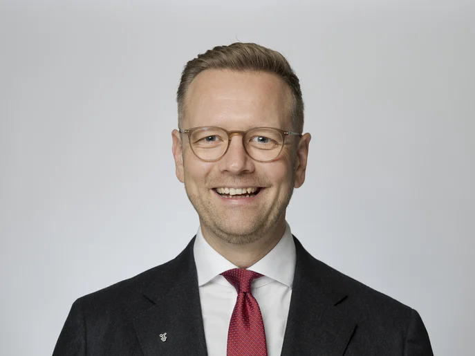 Intendant des Gerhart-Hauptmann-Theaters Görlitz-Zittau in schwarzem Anzug und mit roter Krawatte vor neutralem Hintergrund.