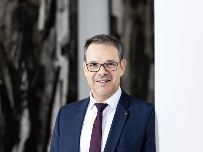 Generalintendant und Geschäftsführer der Städtische Theater Chemnitz gGmbh in blauem Anzug und gestreifter Krawatte vor einer Wand mit abstraktem Muster.